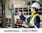 Building inspector man using digital tablet pointing at plumbing pipeline system. Asian male worker in green vest, protective ear muffs and safety helmet working for building maintenance inspection