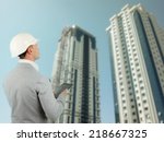 Building inspector or structural engineer wearing a hardhat standing with a tablet computer surveying a newly built office block in a conceptual image