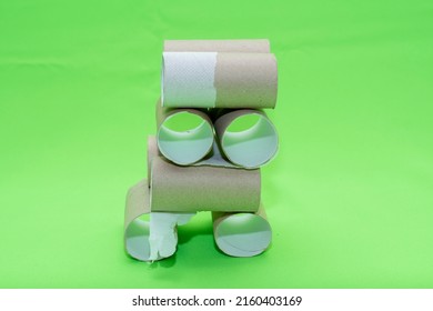 A Building Made Of Empty Toilet Paper Rolls On A Green Background. Background On The Theme Of The Economic Crisis And The Lack Of Items For Basic Needs.