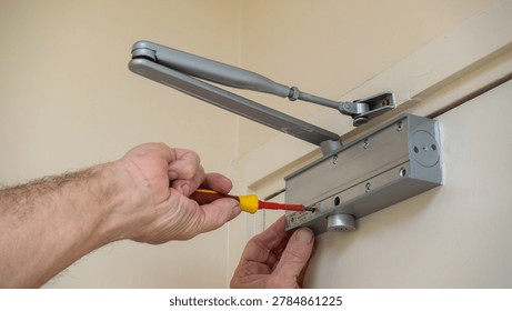 Building maintenance engineer adjusting an automatic door closer on a fire door using a screwdriver. Fire door compliance in commercial buildings.