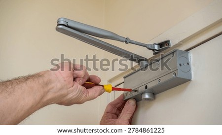 Building maintenance engineer adjusting an automatic door closer on a fire door using a screwdriver. Fire door compliance in commercial buildings.