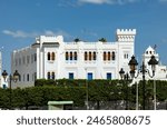 Building Office of Religions in Tunisian capital on Kasbah Square. White building in Arabic style stands out vividly against background of blue sky and green hedge of ornamental shrubs.