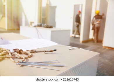 Building plan, eye bolt and screws on plasterboard panels with workers in background - Powered by Shutterstock