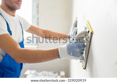 building, profession and people concept - close up of male builder sanding wall indoors