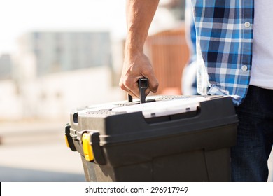 building, protective gear and people concept - close up of builder carrying toolbox at construction site