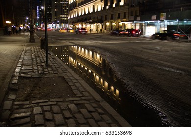 Building reflects on puddle at night street, New York
