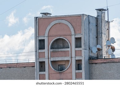 Building section featuring mid-century rounded arches, muted pink facade with white accents, urban setting, satellite dishes, power lines, daytime scene, architectural details