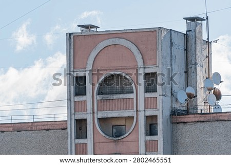 Building section featuring mid-century rounded arches, muted pink facade with white accents, urban setting, satellite dishes, power lines, daytime scene, architectural details