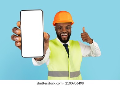 Building Services. Black Male Construction Worker Demonstrating Blank Smartphone And Showing Thumb Up, Smiling African American Man In Safety Vest And Hard Hat Holding Phone With White Screen, Mockup