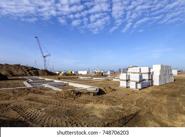 Building Site In The Early Stages, With Foundations For Houses, Building Materials And A Small Crane In The Background