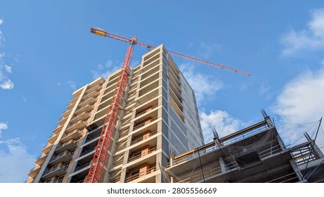 Building skyscraper structure with towering red construction crane reaching into a vast blue sky, representing urbanization, development, investment, and future growth of modern city infrastructure