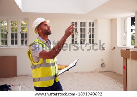 Building Surveyor Wearing Hard Hat With Clipboard Looking At Interior Of New Property