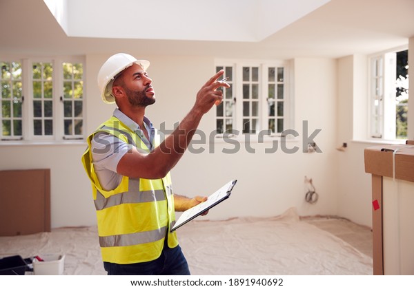 Building Surveyor Wearing Hard Hat With\
Clipboard Looking At Interior Of New\
Property