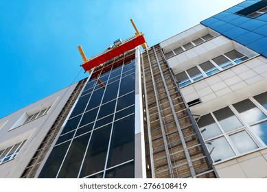 A building under construction with a crane installing glass facade panels.