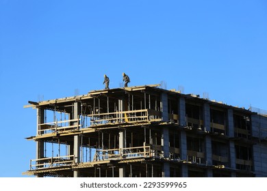 Building under construction! Top of the building against the blue sky with construction workers with yellow protective helmet.  - Powered by Shutterstock