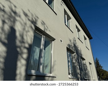 Building wall with multiple windows and tree shadows creating a pattern on its facade