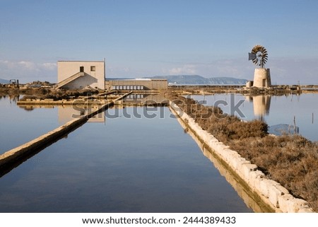 A building and windmill next to salt pans for salt production in the Trapani area in western Sicily, Italy