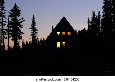 Building in the woods after sunset; windows are lit