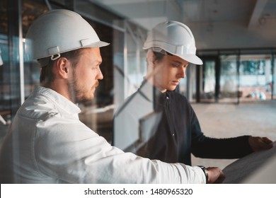 Building Worker And Architect Discussing Build Drawing On Construction Site. Two Industrial Engineers Wearing Safety Hard Hat Have Meeting On Commercial Building Structure