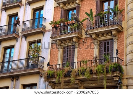 Buildings exteriors in Barcelona city centre with balconies full of tropical plants in pots, decorations,  sculptures of monkeys and people,  big windows,  orange and cream colours,  autumn scene 