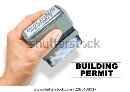 Buildings Permit about building activity and construction industry - concept with hand and plastic stamp with text on white background