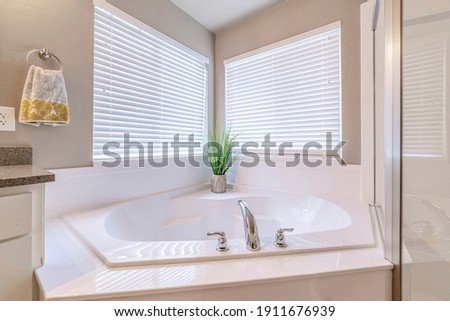 Built in bathtub at the corner of a well lighted home bathroom with two windows