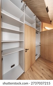 Built-in storage system featuring open wood-paneled cabinets and clean white shelves in a minimalist interior. Hardwood floors and concealed hinges. No logos visible