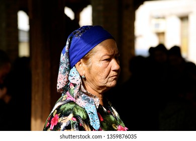 Bukhara, Uzbekistan 20 October 2015. Muslim Woman Portrait. Dressed In Colourful Clothing And Wearing A Colourful Scarf. Older With Wrinkles, Wearing Earrings. Serious Look. Dark Background