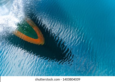 Bulbous bow of the warship sailing through the sea created wave piercing water splash with reflection of its hull and cloud above the blue sky on the ripple water.