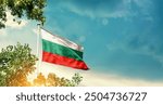 Bulgaria national flag waving in the sky behind the tree. The flag blowing with beautiful sunlight. Bulgaria national flag for independence day.