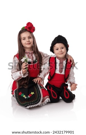 Bulgarian girl and boy in ethnic folklore costumes with spring traditional martenitsa on hands and bouquet of snowdrops, happy Baba Marta day, Bulgaria
