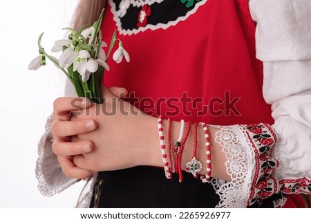 Bulgarian girl in traditional folklore costumes with snowdrop flowers and handcraft wool bracelet martenitsa symbol of Baba Marta, spring and Easter holiday