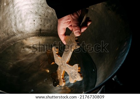 A Bulgarian priest is holding a cross over water for an orthodox baby baptism. High quality photo