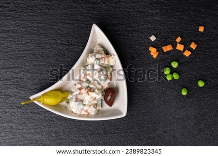 Bulgarian take on traditional Russian salad in small triangular plate on black background with spread diced pickled cucumbers and green peas.