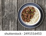 Bulgogi, Korean BBQ Beef, fried thinly sliced beef sprinkled with sesame seeds and spring onion served with long grain rice in bowl on grey rustic wooden table, flat lay, free space