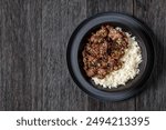 Bulgogi, Korean BBQ Beef, fried thinly sliced beef sprinkled with sesame seeds and spring onion served with long grain rice in black bowl on dark oak wooden table, flat lay, free space