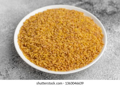 Bulgur in a white saucer on a gray concrete background