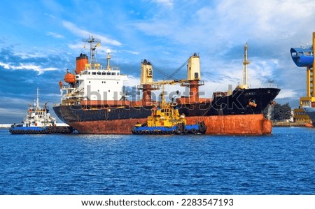 Bulk carrier for transportation of wheat in the waters of the port of Odessa. Two sea tugs moor an old dry-cargo ship in the port of the city of Odessa on the Black Sea, Ukraine