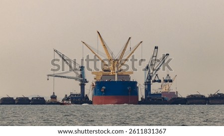 Bulk carrier vessel loading cargo at industrial port with onboard cranes, Maritime cargo operation bulk ship handling goods at seaport, Heavy bulk cargo transfer goods operation at sea.
