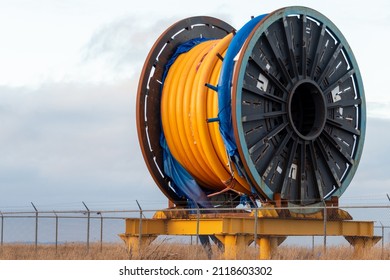 Bulk sub-sea industrial glass fiber optic cable on a metal spool on a ship's stand. The orange data line is coiled around a black reel in a storage yard.Internet communications spool storage yard.