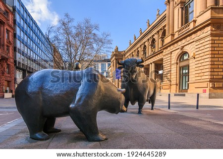 Bull and bear as a symbol figure. Place in front of the building of the Frankfurt Stock Exchange. Commercial buildings with a brown facade in the sunshine and blue sky with clouds 