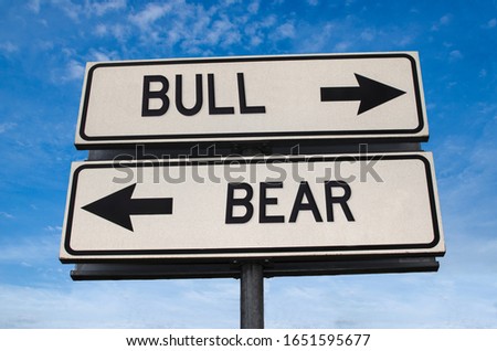 Bull vs bear. White two street signs with arrow on metal pole with word. Directional road. Crossroads Road Sign, Two Arrow. Blue sky background. Two way road sign with text.