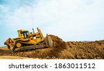 Bulldozer at a construction site shovels mountain soil into a heap