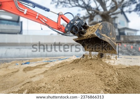Bulldozer digging sand on a sandy beach. Beach Houses and concrete retaining walls on the beach. Auckland.
