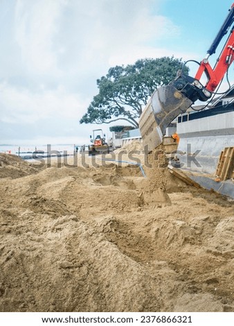 Bulldozer digging sand on a sandy beach. Houses and concrete retaining walls on the beach. Vertical format.  