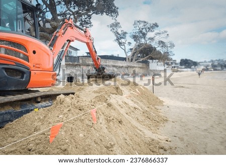 Bulldozer digging sand on a sandy beach. Unrecognizable people walking on the beach. Auckland.  