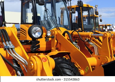 Bulldozer headlight, row of huge orange powerful construction machines, tractors, excavators, focused on spotlight, blue sky and white clouds on background, selective focus 