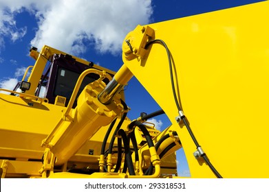 Bulldozer, Huge Yellow Powerful Construction Machinery With Big Bucket, Focused On Hydraulic Piston Arm, Blue Sky And White Clouds On Background