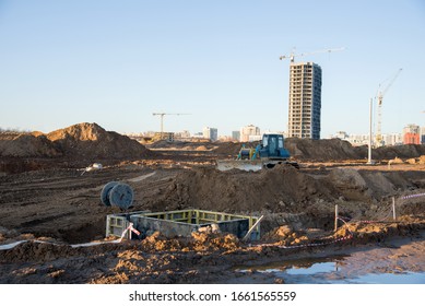 Bulldozer at the large scale construction site on tower cranes background. Installation of concrete sewer wells and pipe drainage in the ground. Water Main and Sanitary Sewer Projects