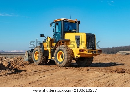 Bulldozer or loader moves the earth at the construction site against the blue sky. An earthmoving machine is leveling the site. Construction heavy equipment for earthworks